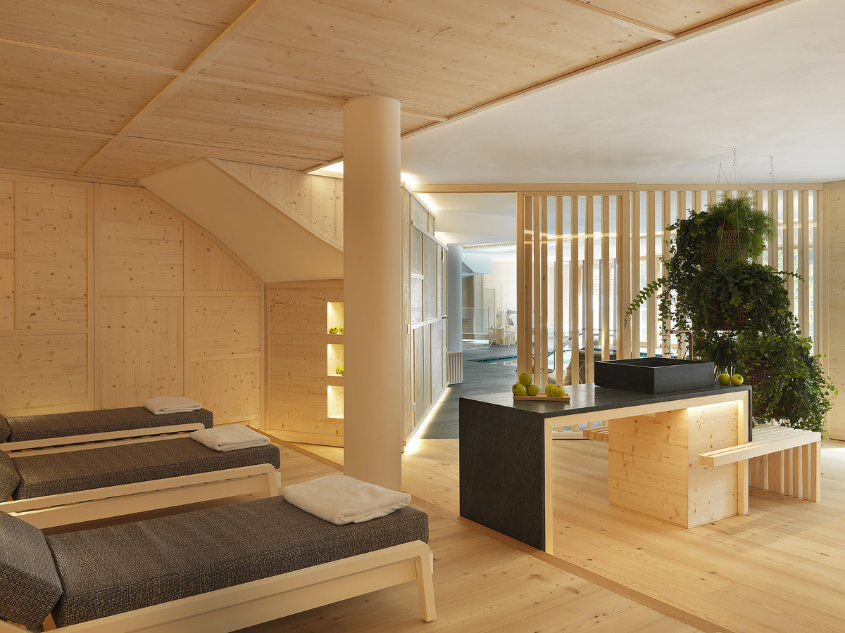 Area relax della spa con lettini e bancone, partizioni in legno a listelli e piante sospese