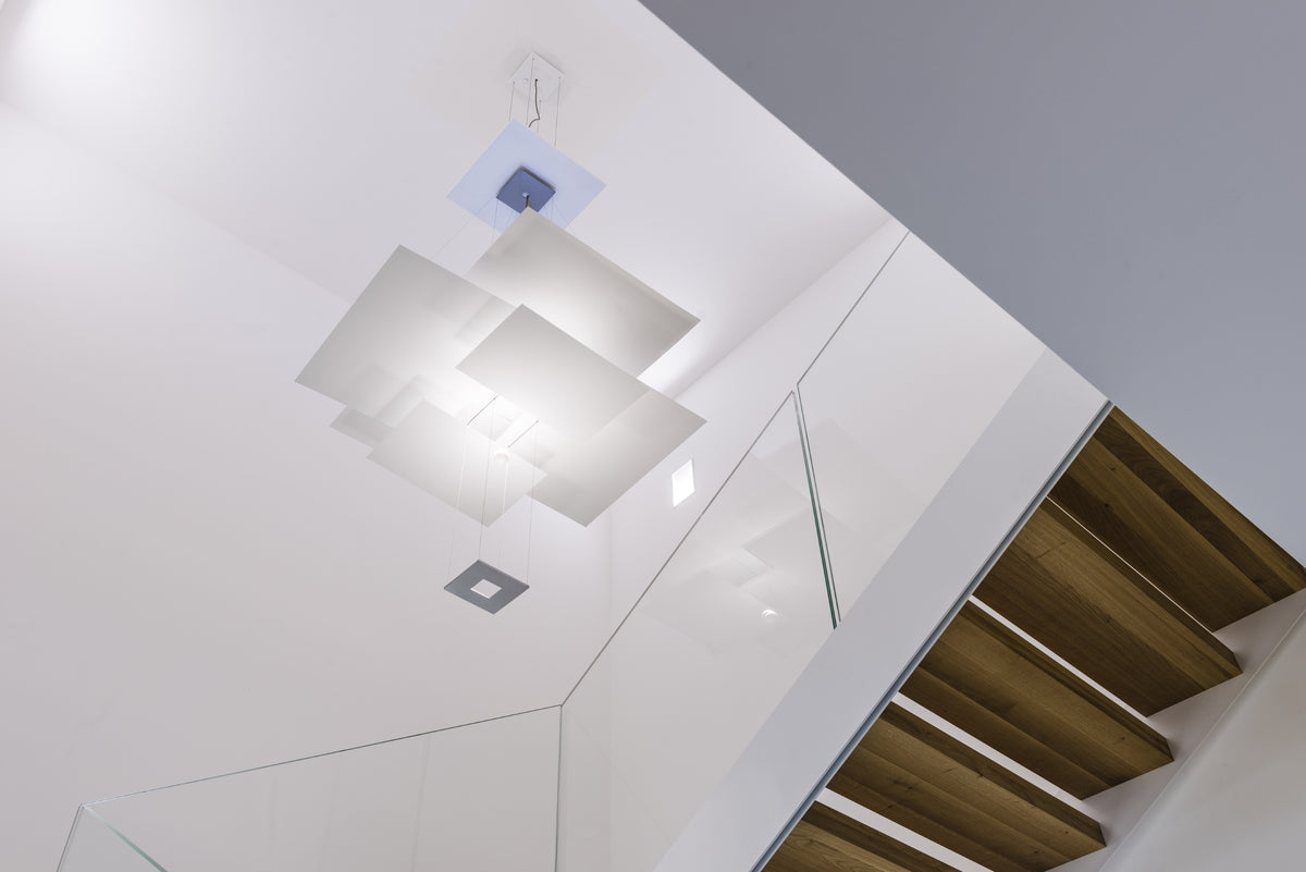 Dettaglio della scala interna in metallo, vetro e legno con lampada di design sospesa Ingo Maurer, spazio luminoso e minimale