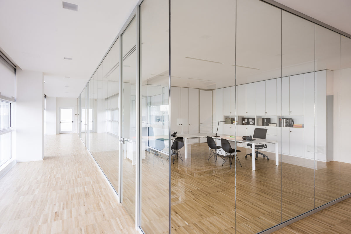 Corridoio vetrato che collega gli uffici operativi, spazio minimale con luce naturale e pavimento caldo in legno