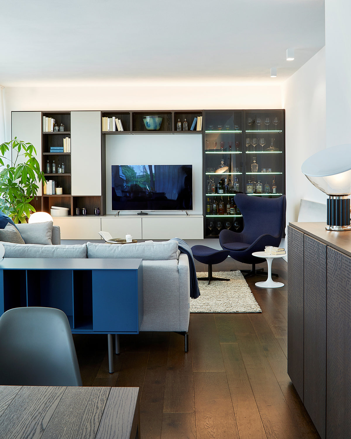 Dettaglio living con divano angolare, poltrona di design blu e parete attrezzata con TV e vetrina integrata con illuminazione interna