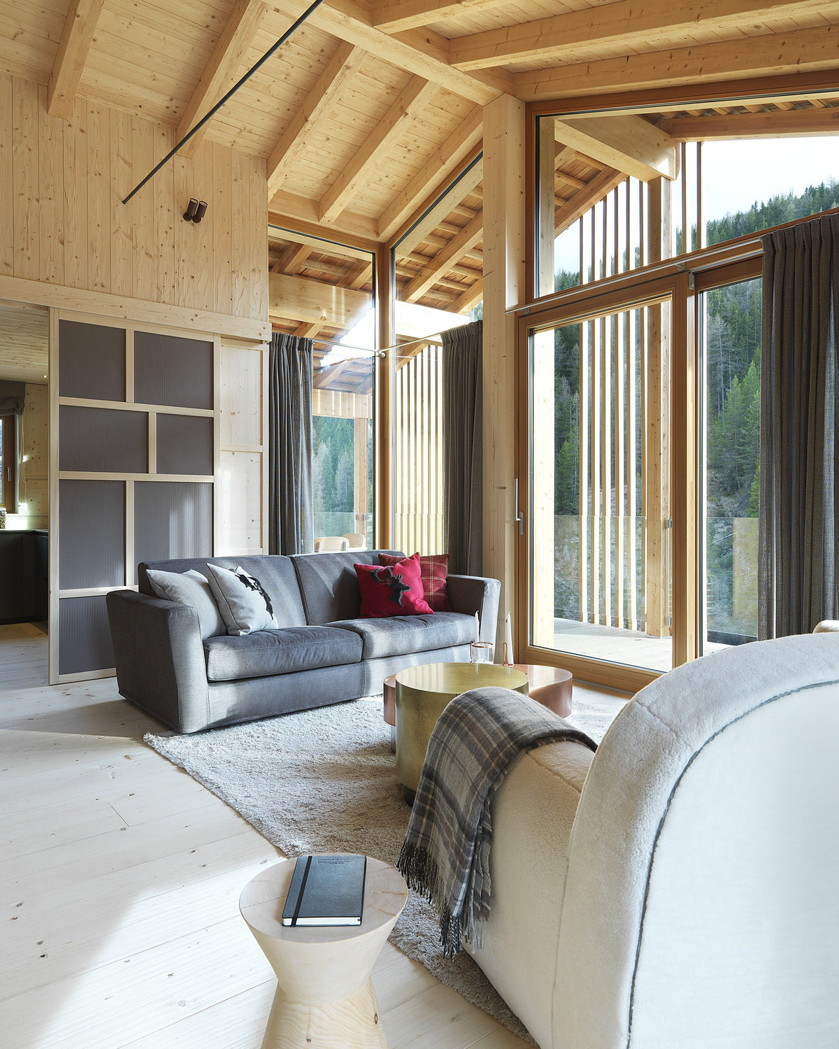 Dettaglio living con divano grigio, coperta e vetrate a tutta altezza
