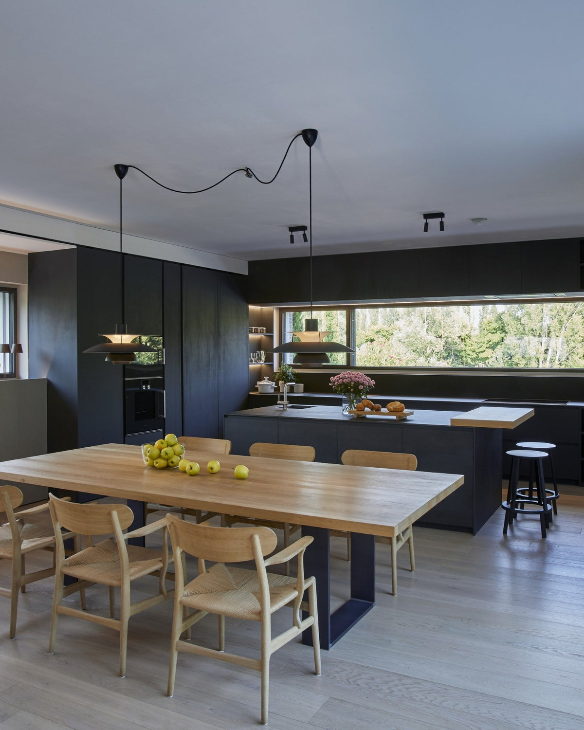 Dettaglio della cucina con isola scura e tavolo in legno nell’open space