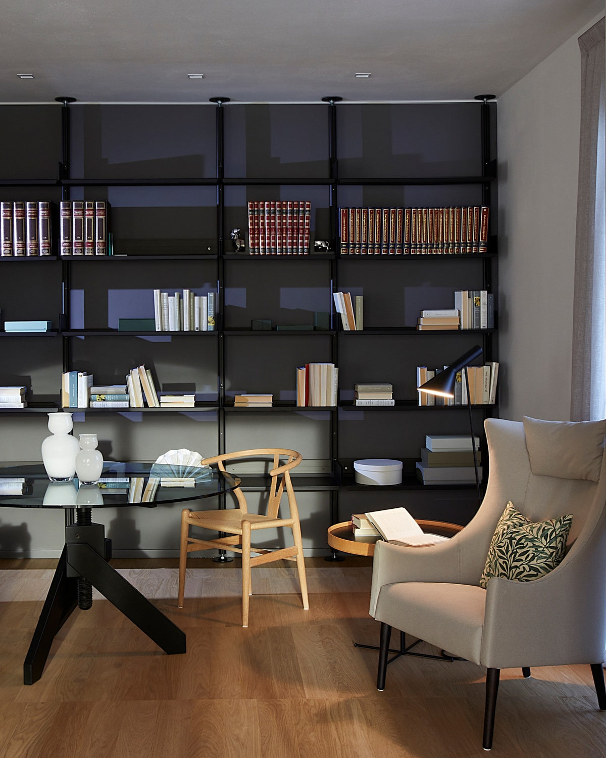 Dettaglio della zona lettura nel living, con libreria a parete, tavolo in vetro e poltrona in pelle