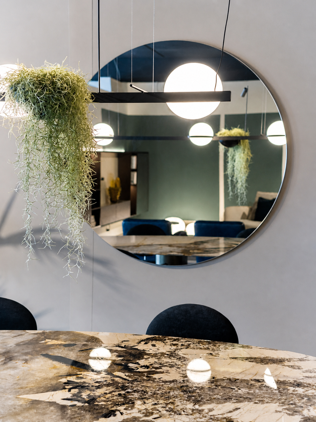 Dettaglio sala da pranzo nello showroom Cariolato con tavolo in marmo decorativo, specchio rotondo e lampada sospesa di design