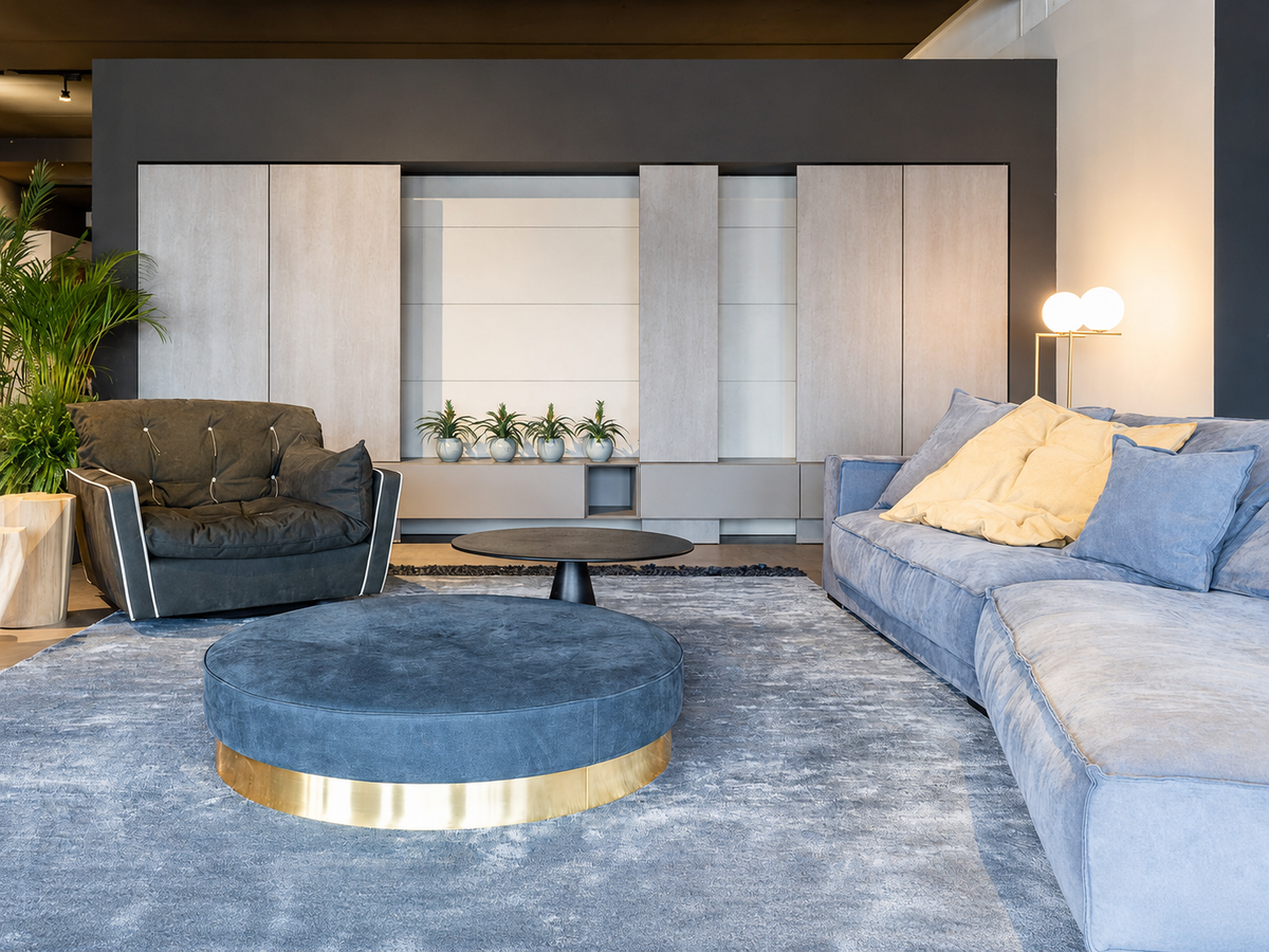 Area living nello showroom Cariolato a Cornedo Vicentino con divano azzurro, poltrona nera, pouf rotondo e parete attrezzata contemporanea